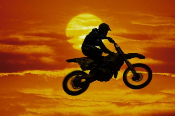 Motocross racer doing jump in front of big sun